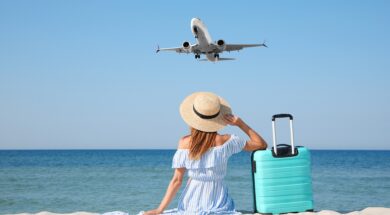 Woman,With,Suitcase,On,Sandy,Beach,Looking,At,Airplane,Flying
